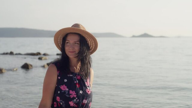 close-up of a girl in a hat smiling walking by the sea. A woman on vacation is happy walking near the ocean. High quality 4k footage