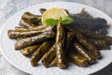 Delicious dolma (sarma) stuffed grape leaves rice, white yogurt sauce. Lebanese dolma sarma on plate. Lebanon turkish greek middle eastern cuisine. (Turkish name; Yaprak sarma)
