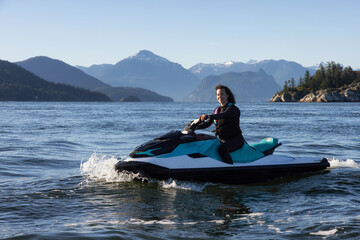 Fototapeta premium Adventurous Caucasian Woman on Water Scooter riding in the Ocean. Howe Sound and mountain landscape in background. West Vancouver, British Columbia, Canada.