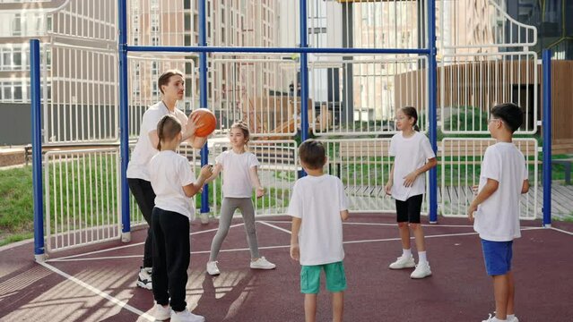 Basketball training session with coach. Teacher playing with children a game with ball in the school yard. Sport and education concept.