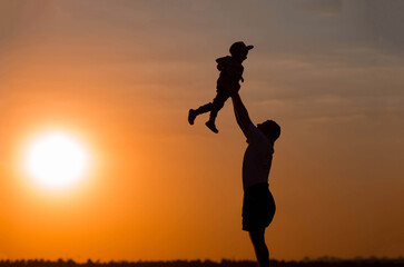 Father and son play in the park during sunset. People have fun in nature. Dark silhouettes of people on an orange background.The concept of a friendly family and summer holidays and Father's Day.