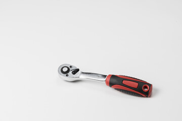 the tool of one gray metal ratchet wrench with a red black plastic handle lies on a white table