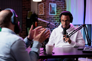 African american influencer recording podcast with guest, using sound equipment at desk. Cheerful...