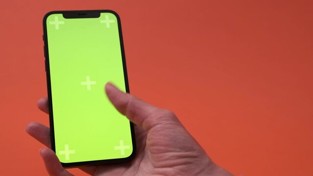 woman hand with smartphone with blank green screen, screen touch copy space for app or website design over red studio background, mockup footage. 