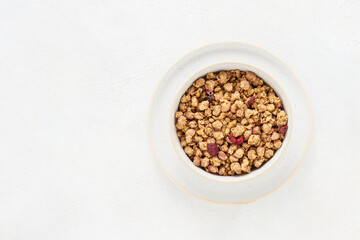 Organic wholegrain granola with dried berries in a bowl on white background. Top view, copy space