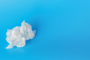 A crumpled white napkin, a used paper handkerchief lies on a blue background - a runny nose, symptoms of illness, garbage, dirt