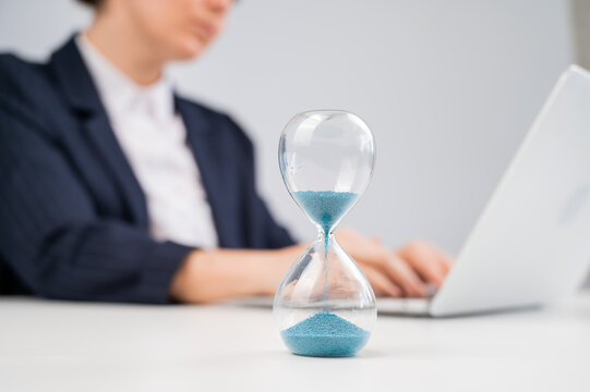 Business woman keeps track of time on an hourglass while working.