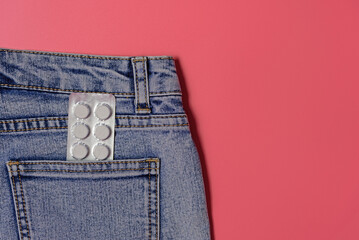 Pack of white pills in the back pocket of jeans on a pink background - health care, women's health,...