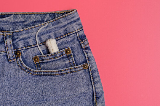 In the front pocket of denim shorts lies a female tampon, blue jeans, feminine hygiene, women's health, pink background, comfort