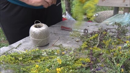 Skillful, old women's hands make a wreath of yellow, white, blue and pink flowers that brings good luck. Near to her is a club with a string and a knife.