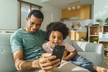 Black African American father and son using smartphone at home. Happy smiling African Man and...