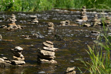 Fototapeta na wymiar River with stream, plants and rock sculptures (Piles of stones) in sunny summer day