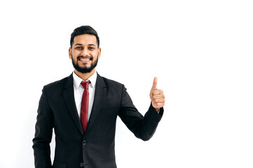 Successful handsome confident indian or arabian businessman in a black business suit, standing over isolated white background, showing thumb up, agree sign, looking at camera, smiling happily
