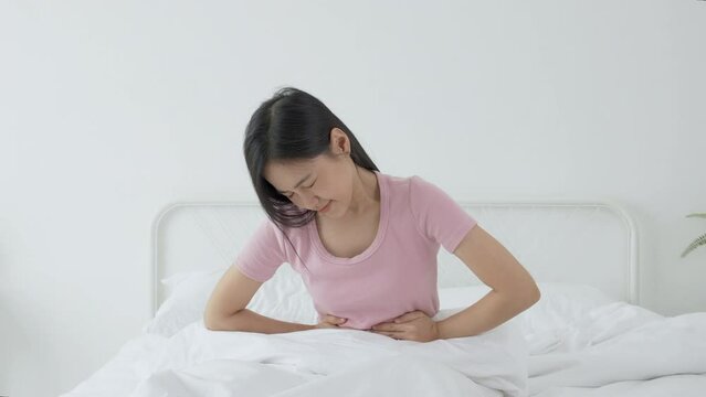 Young asian woman sitting on bed pain stomach or bowel with disease constipation in the bedroom at home, unhappy female sick and menstruation and stomachache, medical and health concept.