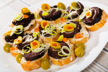 Dish of canape from blood sausage with olives, onion and bread served at plate