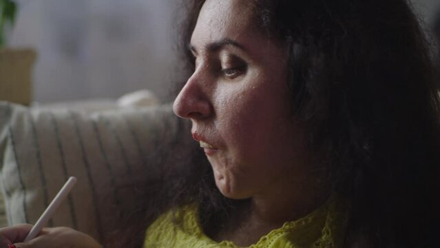 Woman with a physical disability using application for drawing illustrations with pen on a digital tablet computer sitting at home on a sofa