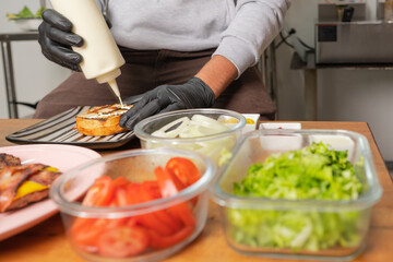 cook adding mayonnaise to the bun for a burger