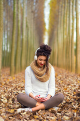 Naklejka na ściany i meble Young woman listening music through headphones while sitting in autumn leaves
