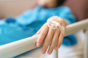 Asia patient woman lying on the bed with saline solution and syringe line on her hand in hospital ward. Raise hand to grab the rails on the edge of the bed. Healthcare and medical concept