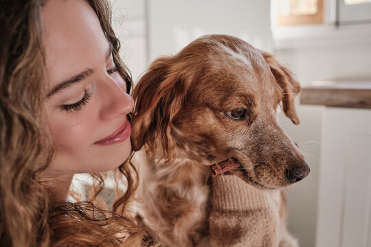 Happy Young Female Owner With Curly Hair Smiling And Looking To Cute Brown Dog At Home