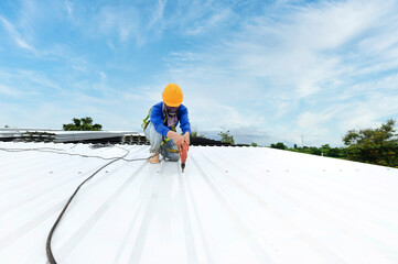 Construction worker in work clothes installing new roofing tools roofing tools, electric drill, and use on new wooden roofs with metal sheets.