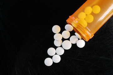  white color medical pills spilling from a orange color container on black 