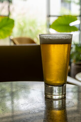 glass of beer on a terrazzo table, two yellow chairs in the background, retro table, window with natural light