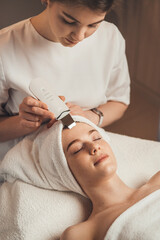 Cosmetologist with ultrasonic scrubber working with woman's face skin. Ultrasound cosmetology...