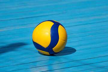Yellow volleyball on volleyball court. The floor is made of wood and covered with blue paint.