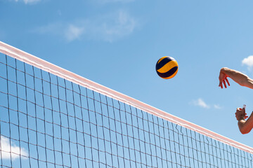 Volleyball flying through air with hands visible against background of a blue sky with clouds