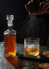 Bottle and glass of whiskey with ice with drops, black background