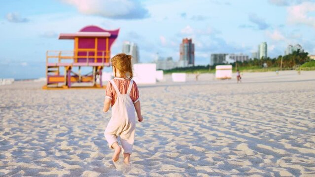 little baby girl running on sandy beach, enjoys summer vacation in Miami Beach