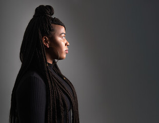 dramatic right side profile portrait of young afro latin woman dressed in black and wearing braided hairstyle on gray studio background. High quality photo