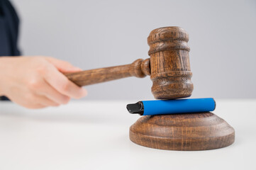 Judge hammering disposable vape with referee's gavel on white table. 