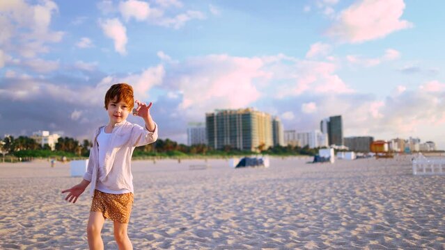 redhead kid, boy having fun on sandy beach, playing with a sea shell on summer vacation. Miami Beach