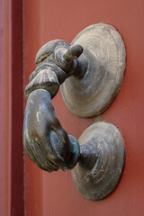 Closeup view of beautiful vintage brass door knocker in shape of hand holding ball isolated on ancient orange red wooden door, Montpellier, France