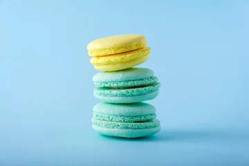 Fotobehang Colorful french macarons cookies (macaroons) on blue background. Dessert, vegetarian sweets close up, stacked balance © Elena