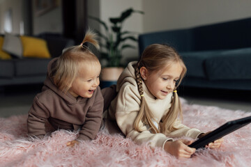 Caucasian siblings using tablet at home. Distance or remote learning for child. Pretty stylish...