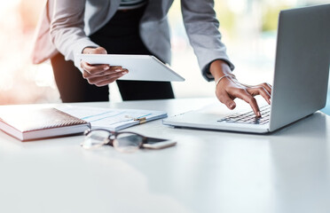 Reading, sending or checking an email or report while at work in at a professional desk. Hands typing on a laptop keyboard and holding a tablet with a business woman working in her corporate office.
