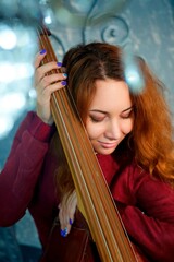 The girl in the red dress standing in the Studio holding a musical instrument the double bass.