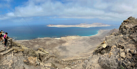 Aerial and Amazing view of beautiful volcanic island Hikers watch La Graciosa island. Panoramic view near Famara Risco, Lanzarote. Location: north of Lanzarote, Canary Islands, Spain. Ocean view.