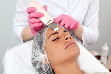 Beauty doctor with ultrasonic scraber doing procedure of ultrasonic cleaning of face. Cosmetology...