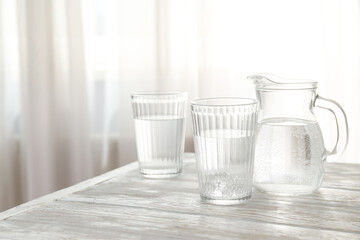 Jug and glasses of water on white wooden table - obrazy, fototapety, plakaty