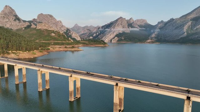 Aerial cinematic drone shot following a group of motorcyclists heading out on a morning adventure crossing the Ria&ntilde;o bridge at sunrise surrounded by the spectacular Cantabrian mountains, Leon, Spain