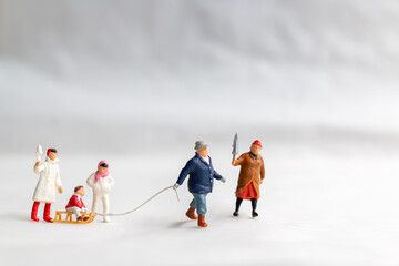 Miniature people Happy family ride a sleigh with snow background, Christmas eve celebration concept.