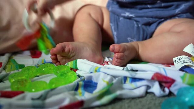 Close up of baby feet while infant is playing with rattle, teething ring on blanket