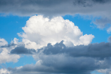 Wild stormy beautiful blue sky with white gray contrasts. Fluffy cumulus clouds in different layers. Concept of struggle between good and evil, bad ot fine weather, wind change in cyclone. Copy space.