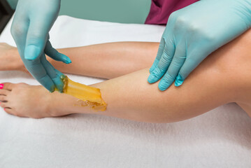 Fototapeta premium Woman undergoing leg hair removal procedure with sugaring paste in salon