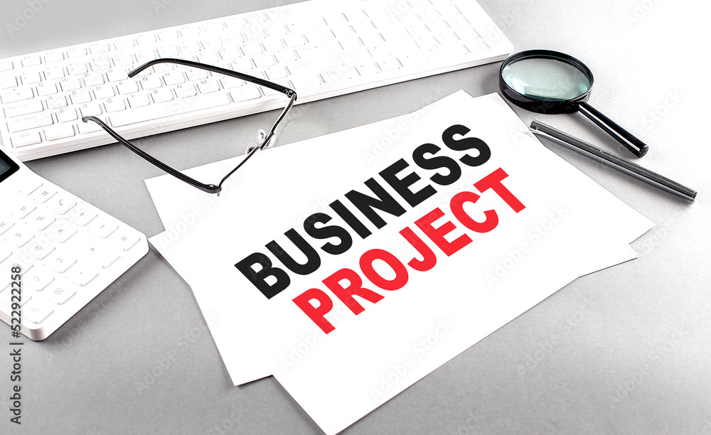 Aufkleber business project text on a paper on a gray background near a calculator and a white keyboard