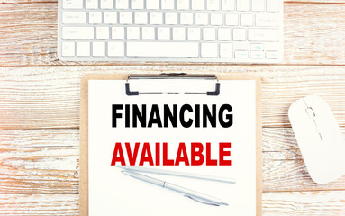 FINANCING AVAILABLE text on a clipboard with keyboard on wooden background
